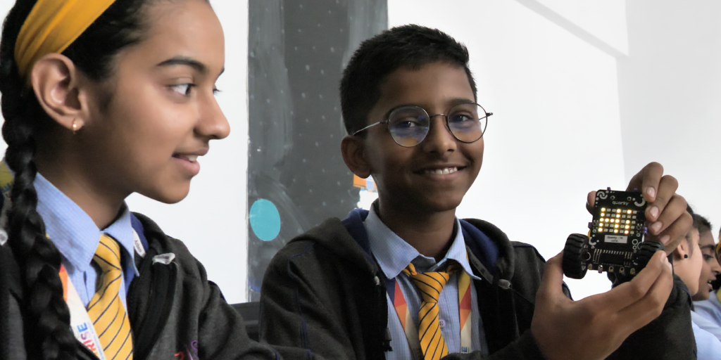 Two students in school uniforms exploring a Quarky reprogrammable robot's LED feature together in a classroom