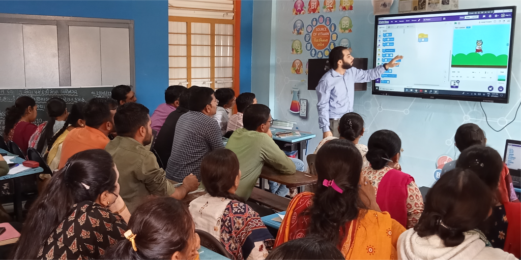 STEM trainer demonstrating a PictoBlox coding lesson to a group of educators in a classroom using a digital smart board